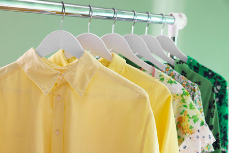 Different women's clothes hanging on rack against green background, closeup