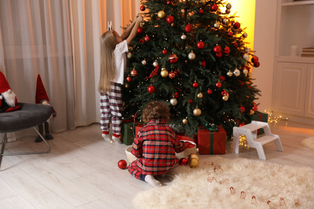 Little children in pajamas decorating Christmas tree at homeの写真素材