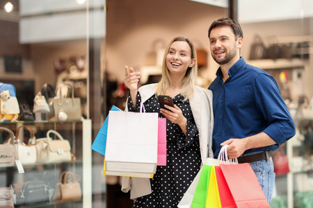 Happy couple with shopping bags and smartphone walking in mall