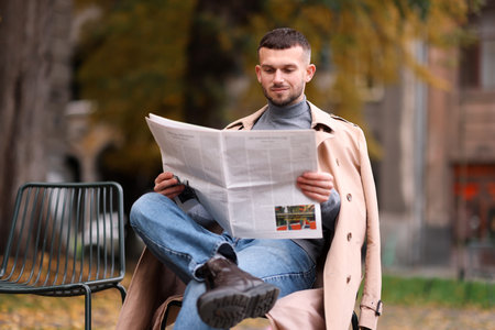 Young man reading newspaper on chair outdoorsの写真素材