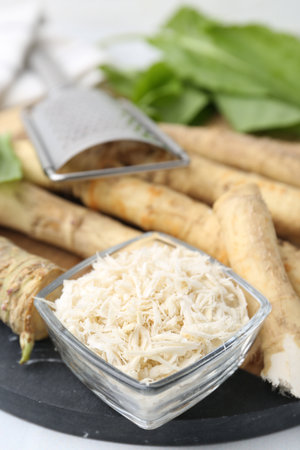 Whole and grated horseradish roots, grater and green leaves on table, closeupの写真素材