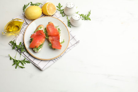 Tasty bruschettas with salmon and arugula served on white marble table, flat lay. Space for textの写真素材