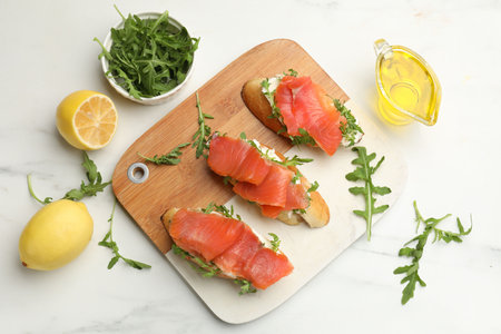 Tasty bruschettas with salmon and arugula served on white marble table, flat layの写真素材