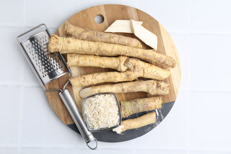Whole and grated horseradish roots near grater on white tiled table, top viewの写真素材