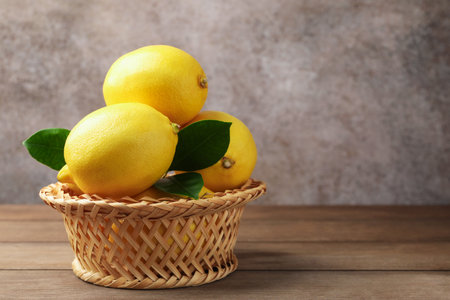 Fresh lemons with green leaves in wicker basket on wooden table against gray textured background, closeup. Space for textの写真素材