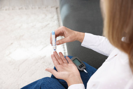 Diabetes. Woman checking blood sugar level with lancet pen on sofa indoors, closeup. Space for textの写真素材