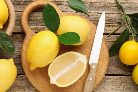 Whole, cut lemons with green leaves and knife on wooden table, flat layの写真素材