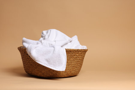 Wicker basket full of laundry on light brown background.の写真素材