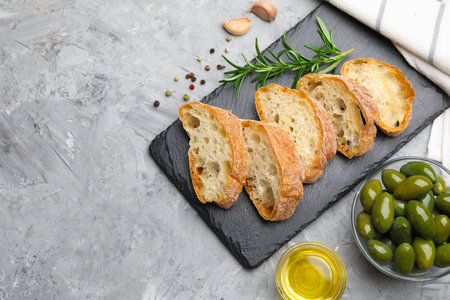 Slices of ciabatta, spices and olives on gray table, flat lay. Space for textの写真素材