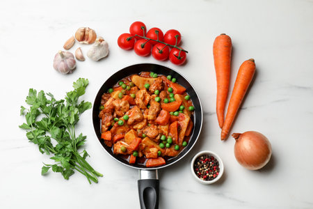 Delicious cooked stew in frying pan and ingredients on white marble table, flat layの写真素材