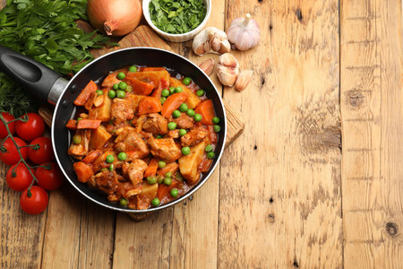 Delicious cooked stew in frying pan and ingredients on wooden table, flat lay. Space for textの写真素材