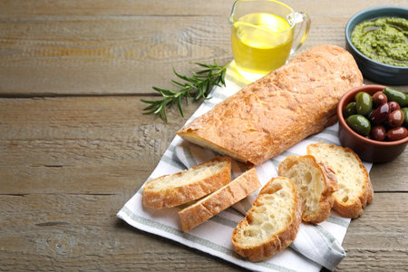 Cut ciabatta, spices and olives on wooden table, closeup. Space for textの写真素材