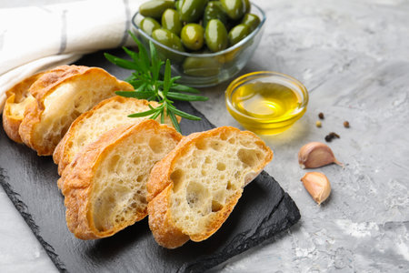 Slices of ciabatta, spices and olives on gray table, closeupの写真素材