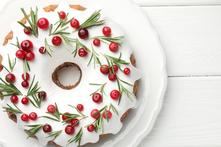 Tasty Christmas cake with icing, cranberries and rosemary on white wooden table, top viewの写真素材