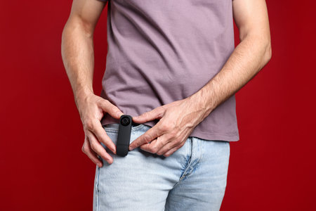 Man with hidden spy camera in his pocket on red background, closeup