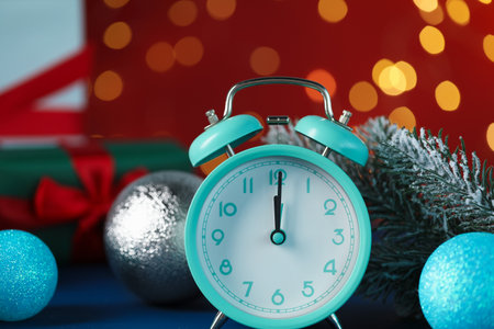 Alarm clock, fir tree branches and baubles on blue table against red background with blurred lights,...