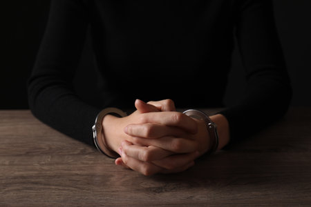 Woman in metal handcuffs at wooden table, closeupの写真素材