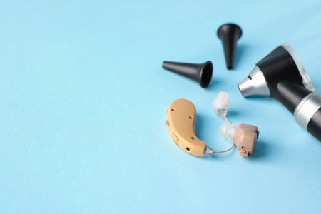 Modern otoscope, hearing aid and ear speculums on light blue background, closeup. Space for textの写真素材