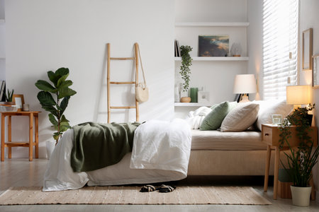Stylish bedroom with large bed, pillows, houseplants and lamp. Interior designの写真素材