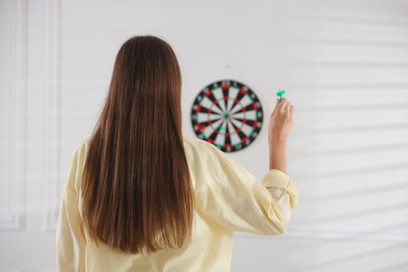 Woman with dart aiming at dartboard indoors, back viewの写真素材
