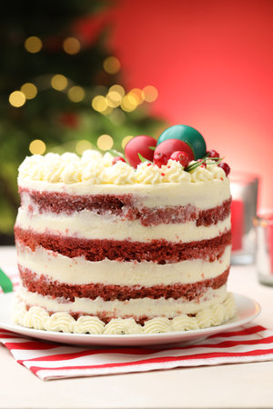 Delicious sponge cake with Christmas decor on white table against red background with blurred...