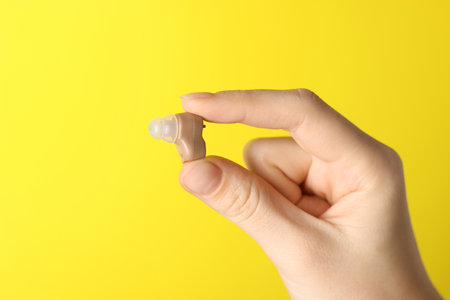 Woman with hearing aid on yellow background, closeup. Space for textの写真素材