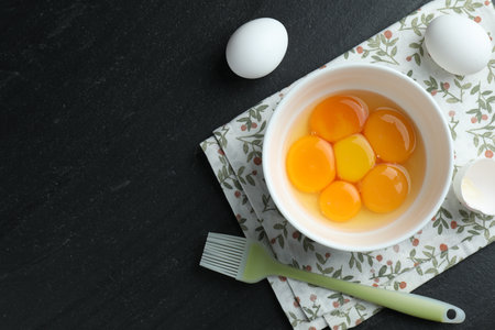 Raw eggs, yolks and brush on black table, flat lay. Space for textの写真素材