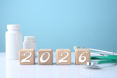 New 2026 year. Cubes with numbers, pills and stethoscope on table against light blue background