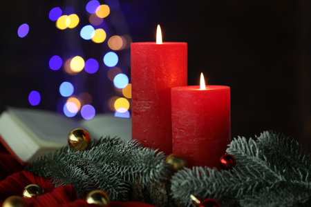 Burning candles, fir tree branches, baubles and sweater against black background with blurred lights, closeup. Bokeh effectの写真素材