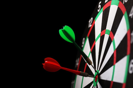 Dartboard with darts on black background, closeup. Space for text