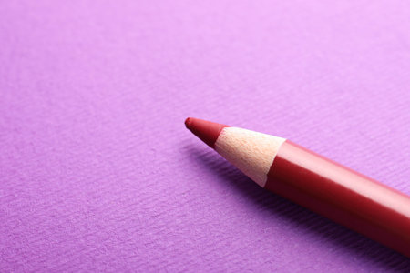 Red eye pencil on purple background, closeup. Space for textの写真素材