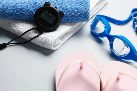 Flip flops, towels, goggles and digital stopwatch on light gray background, closeupの写真素材