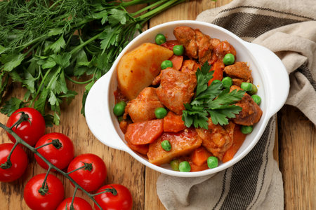 Delicious cooked stew in bowl and ingredients on wooden table, flat layの写真素材