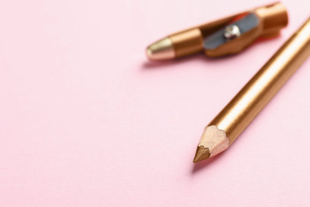 Golden eye pencil and sharpener on pink background, closeup. Space for textの写真素材