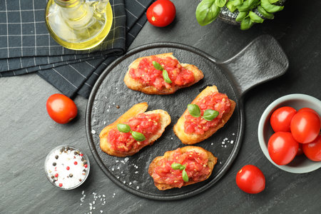 Tasty bruschettas with tomatoes and basil served on black table, flat layの写真素材