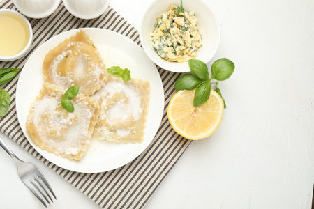 Delicious ravioli with cream sauce and basil served on white table, flat lay. Space for textの写真素材
