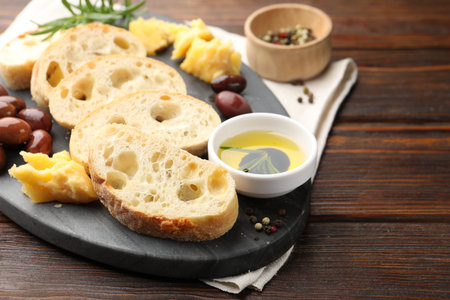 Pieces of fresh ciabatta, butter, olives, cheese and peppercorns on wooden table, closeup. Space for textの写真素材