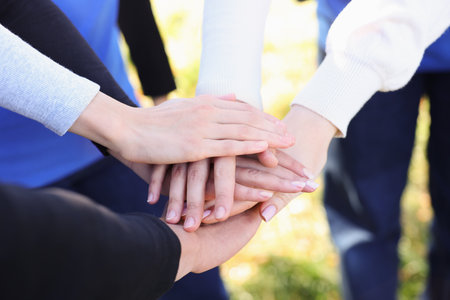 Group of volunteers stacking hands outdoors, closeup