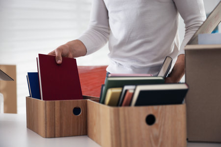 Moving day. Young man putting books into boxes at table in office, closeupの写真素材