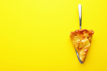 Piece of delicious homemade apple pie and spatula on yellow background, top view. Space for textの写真素材