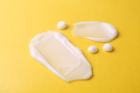 Samples of moisturizing creams on yellow background, closeup