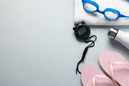 Flip flops, towel, goggles, bottle and digital stopwatch on light gray background, flat lay. Space for textの写真素材