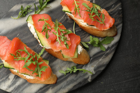 Tasty bruschettas with salmon, cream cheese, cucumber and arugula on black table, top viewの写真素材