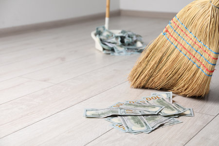 Sweeping dollar banknotes with broom into dustpan on light wooden floor, selective focus. Space for textの写真素材