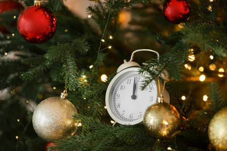 New Year greeting card. Alarm clock, festive lights and shiny baubles on fir tree branches, closeup. Bokeh effectの写真素材