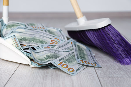 Sweeping dollar banknotes with broom into dustpan on light wooden floor, closeupの写真素材