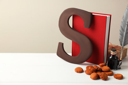 Sinterklaas (Saint Nicholas) Day. Chocolate letter S, kruidnoten cookies, gift and notebook with feather on white table. Space for textの写真素材