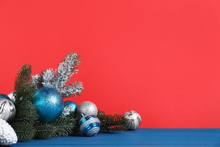 Beautiful Christmas composition with fir tree branches and festive decor on blue wooden table against red background, closeup. Space for textの写真素材