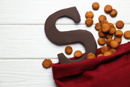 Sinterklaas (Saint Nicholas) Day. Sack with kruidnoten cookies and chocolate letter S on white wooden background, flat lay. Space for textの写真素材