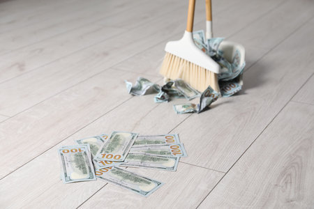 Sweeping dollar banknotes with broom into dustpan on light wooden floor, selective focus. Space for...